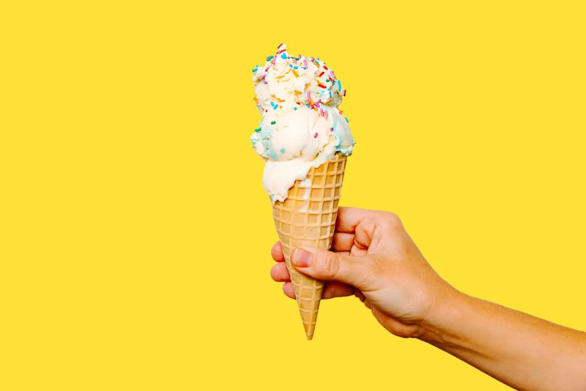 Hand hält Eiswaffel vor gelbem Hintergrund